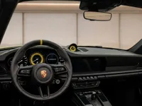 The luxurious cockpit of the 2025 Porsche 911 Turbo S Cabriolet in Zurich, featuring the steering wheel and dashboard with yellow stitching.