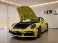 A yellow Porsche 911 Turbo S Cabriolet with its front trunk open, showcased in a modern showroom in Zurich.