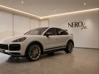 The white Porsche Cayenne Turbo GT is showcased from a front three-quarter view inside the modern Nero Line showroom in Zurich.