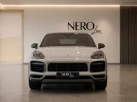 The sleek front view of the 2022 Porsche Cayenne Turbo GT in gloss Chalk, showcased in a modern Zurich showroom.