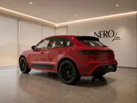 The red Porsche Macan GTS is shown from a rear three-quarter angle inside a modern showroom in Lausanne.