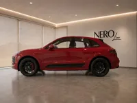 The red Porsche Macan GTS is parked in a showroom, viewed from its left side profile, showcasing its sleek design.