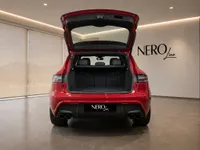 The vibrant red Porsche Macan GTS is shown from the rear with its trunk open, revealing ample cargo space in a showroom in Lausanne.