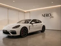 The white 2024 Porsche Panamera 4S E-Hybrid is showcased in a modern showroom with the Nero Line logo in Lausanne.