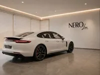 The white 2024 Porsche Panamera 4S E-Hybrid is seen from a rear three-quarter angle in a modern showroom in Lausanne.