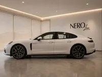 The white 2024 Porsche Panamera 4S E-Hybrid is elegantly displayed from a side view in a modern showroom in Lausanne.