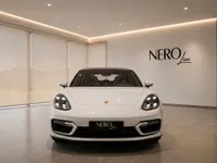 Front view of the white 2024 Porsche Panamera 4S E-Hybrid in a modern showroom in Lausanne, featuring the NEROline logo.