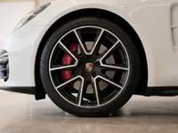 Close-up of the front wheel of a white Porsche Panamera, showcasing the black multi-spoke rim with red brake calipers in Lausanne.