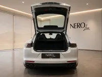 The rear view of a white Porsche Panamera 4S E-Hybrid with its trunk open, showcased in a modern Lausanne showroom.