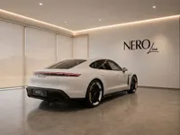 The white Porsche Taycan Turbo is showcased from a rear three-quarter angle in a modern luxury showroom in Lausanne.