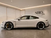 The white Porsche Taycan Turbo is showcased in a modern Lausanne showroom, viewed from its sleek side profile.