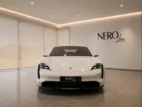 The white Porsche Taycan Turbo is prominently displayed in a modern showroom, facing forward in Lausanne.