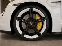 The front wheel of a white Porsche Taycan in Lausanne, showcasing its black and white rim and striking yellow brake caliper.