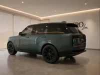 The gloss dark green Land Rover Range Rover is showcased from a rear three-quarter angle in a modern showroom in Lausanne.