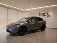 The 2021 Tesla Model X in satin Stealth Grey, shown from a front three-quarter view, parked in a modern showroom in Lausanne.
