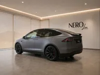 The satin Stealth Grey Tesla Model X is showcased from a rear three-quarter angle in a modern showroom in Lausanne.