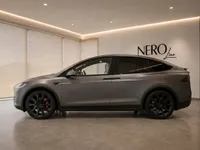 The satin Stealth Grey Tesla Model X is showcased from its side profile in a modern Nero Line showroom in Lausanne.