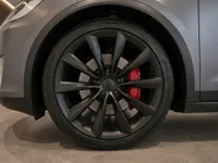 Close-up of the Tesla Model X's front wheel, showcasing the matte black rim and vibrant red brake calipers.