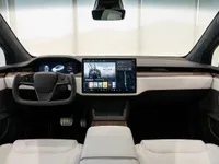 The modern interior of the Tesla Model X in Lausanne features a yoke steering wheel, a large central touchscreen, and white leather seats.