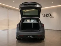 The satin Stealth Grey Tesla Model X is shown from the rear with its trunk open, revealing the spacious cargo area and folded seats in Lausanne.