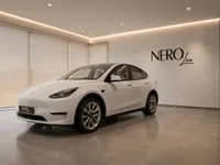 The gloss white Tesla Model Y is showcased in a modern showroom, captured from a front three-quarter angle in Lausanne.