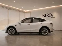 A white Tesla Model Y is parked in a modern showroom, showcasing its sleek side profile and the NEROline logo on the wall.