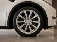 The white Tesla Model Y's front wheel with silver multi-spoke rims is visible in Lausanne.