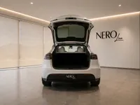 The white Tesla Model Y is shown from the rear with its trunk open, highlighting the spacious cargo area in Lausanne.