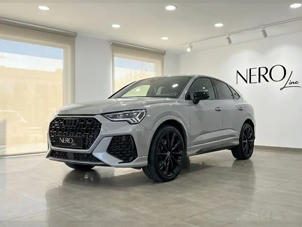 메탈릭 실버 2023 아우디 RSQ3가 바르셀로나 실내에서 전면 쿼터 앵글로 전시되어 있습니다.