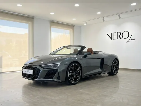 The metallic gray 2023 Audi R8 V10 Spyder Performance convertible, with its top down and brown interior, is showcased in a showroom in Marbella.