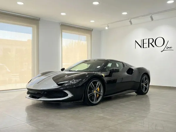 A black and silver 2024 Ferrari 296 GTB is showcased in a modern showroom in Madrid, viewed from the front three-quarter angle.