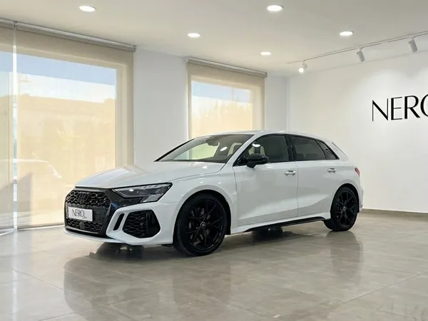 The pearl white Audi RS3 is showcased from a front three-quarter angle in a modern Nero Line showroom in Marbella.