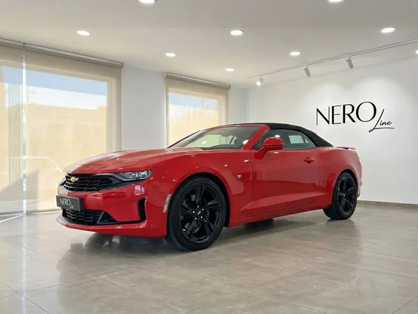 Un llamativo Chevrolet Camaro convertible rojo se exhibe desde un ángulo frontal tres cuartos en una moderna sala de exposición en Alicante.
