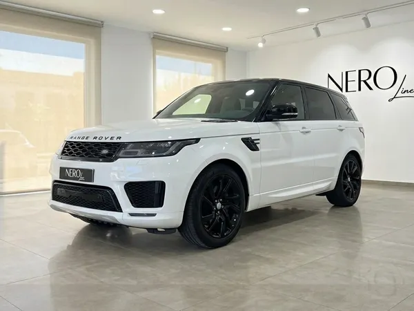 Un Range Rover Sport blanco con techo y llantas negras está aparcado en un concesionario en Barcelona, visto desde un ángulo frontal de tres cuartos.