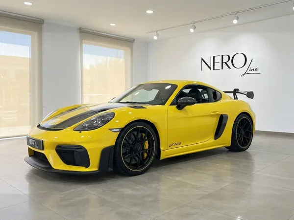 تُعرض سيارة بورش 718 كايمان GT4 RS الصفراء الزاهية من زاوية أمامية ثلاثية الأرباع في صالة عرض حديثة في أليكانتي.