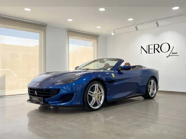 The metallic blue 2022 Ferrari Portofino convertible is showcased from a front three-quarter view in a showroom in Malaga.
