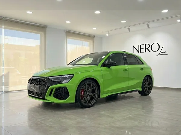 The 2023 Audi RS3 Sportback in gloss Kyalami Green is shown from a front three-quarter view inside a Marbella showroom.