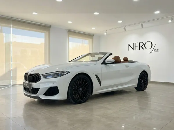 흰색 BMW M850i 카브리올레가 컨버터블 탑을 내리고 고급스러운 갈색 인테리어를 자랑하며 알리칸테 쇼룸에 우아하게 전시되어 있습니다.