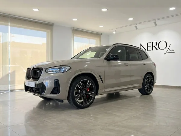 글로스 듄 그레이 색상의 2025년형 BMW X3 M50i xDrive가 마르베야의 쇼룸에서 전면 쿼터 앵글로 전시되어 있습니다.