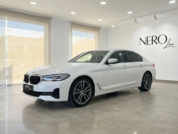 2022년형 흰색 BMW 530e xDrive가 알리칸테의 쇼룸에서 전면 쿼터 앵글로 전시되어 있습니다.
