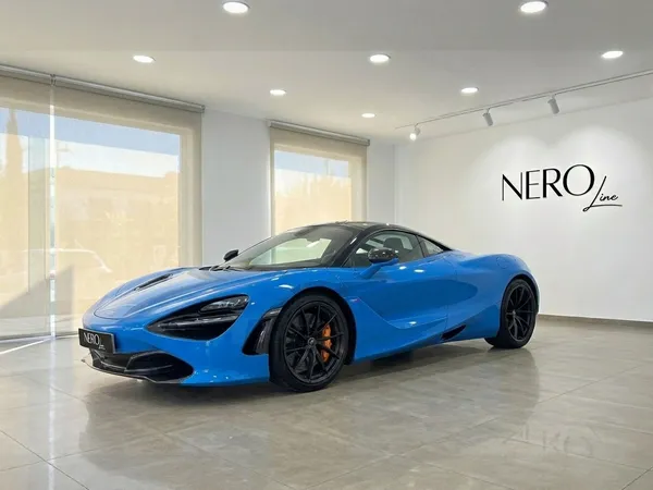 선명한 파란색 McLaren 720S 슈퍼카가 마르베야의 큰 창문이 있는 쇼룸에 주차되어 있습니다.