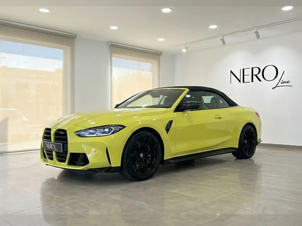 유광 상파울루 옐로우 2022 BMW M4 컴페티션 컨버터블 xDrive, 검은색 소프트탑이 마르베야 실내에 주차되어 있으며, 전면 3/4 모습입니다.