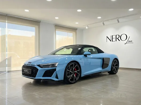 A light blue Audi R8 Spyder convertible is showcased from a front three-quarter view inside a showroom in Madrid.