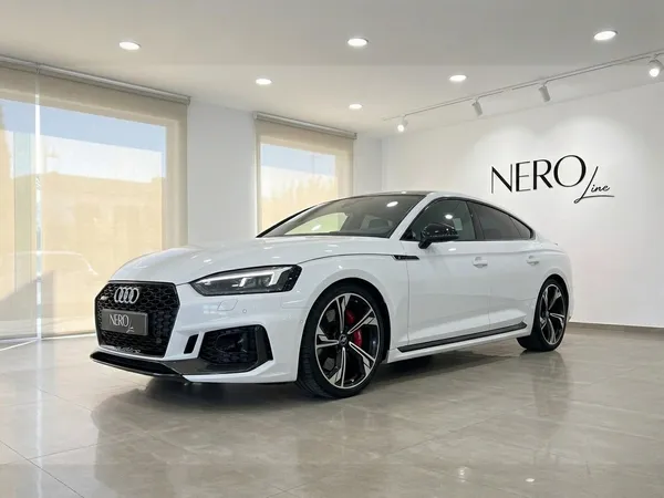 The white Audi RS5 is showcased from a front-three-quarter angle in a modern showroom with the Nero Line logo in Alicante.