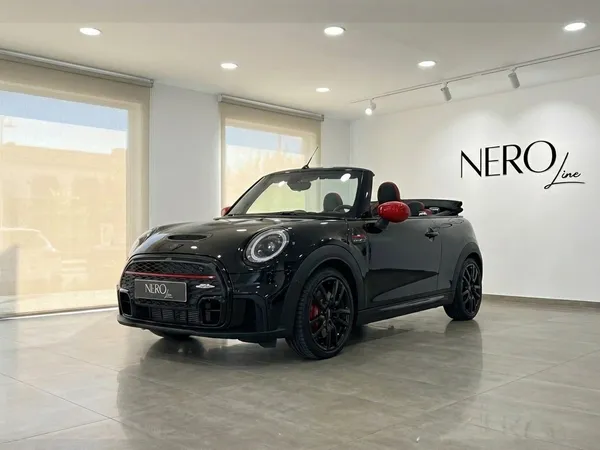 El Mini John Cooper Works Cabrio negro con detalles rojos se exhibe en un concesionario de Barcelona, visto desde un ángulo frontal tres cuartos.