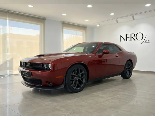 El Dodge Challenger V6 2023 naranja quemado se exhibe desde un ángulo frontal de tres cuartos en un luminoso showroom de Alicante.