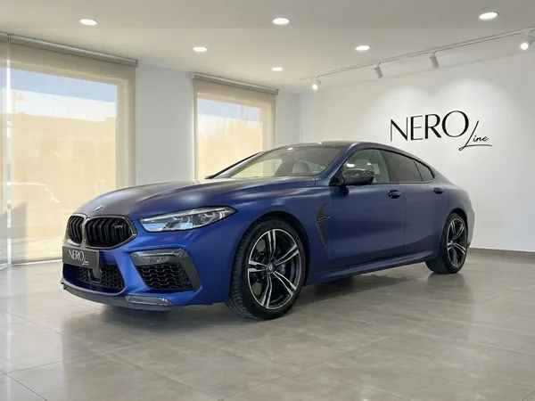 무광 파란색 BMW M8 컴페티션 그란 쿠페가 마르베야의 현대적인 쇼룸에서 전면 쿼터 뷰로 전시되어 있습니다.