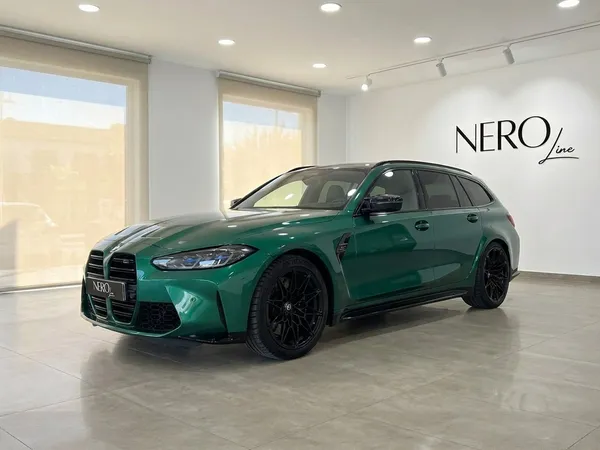메탈릭 아일 오브 맨 그린 BMW M3 투어링 컴페티션 xDrive가 마르베야 쇼룸에서 전면 쿼터 앵글로 전시되어 있습니다.