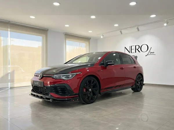 El Volkswagen Golf GTI Clubsport en rojo Kings Red metálico brillante se exhibe desde un ángulo frontal tres cuartos en un moderno concesionario en Alicante.