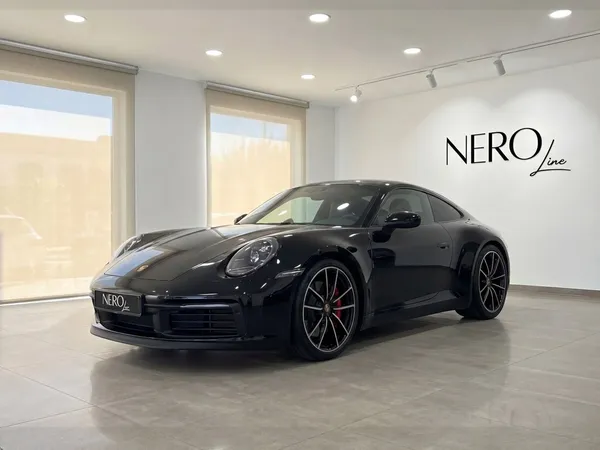 A sleek black Porsche 911 is showcased from a front three-quarter angle in a bright Nero Line showroom in Malaga.